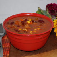 Italian Vegetable Soup in a red bowl with spoon, napkin and sunflowers behind it