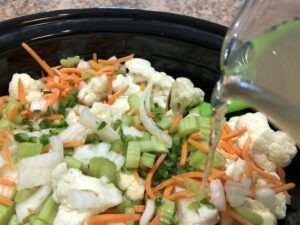 Pouring chicken broth into pot of cauliflower