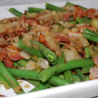Green Beans in a casserole dish topped with cooked bacon and sauted onions