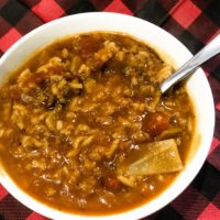 Cabbage Roll Soup on a buffalo check background in a white bowl with a spoon in the soup