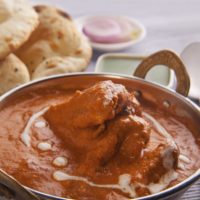 Butter Chicken in a dish with naan in the background