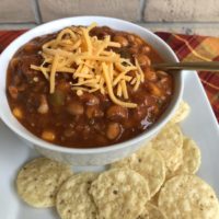 Taco Soup in a white bowl with shredded cheddar on top and tortilla chips on the side.