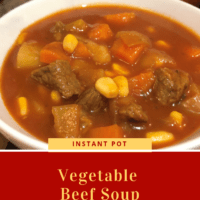 A white bowl with tomato beef broth with pieces of tender beef, corn, carrots and potatoes