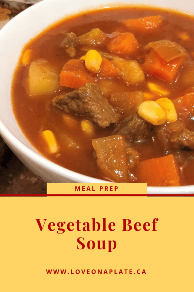 A white bowl with tomato beef broth with pieces of tender beef, corn, carrots and potatoes