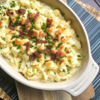 Cauliflower baked in a red casserole dish topped with bacon and cheese