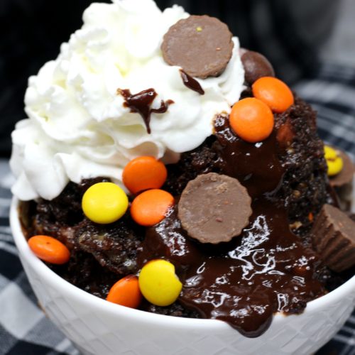 Close up of a white bowl filled with chocolate peanut butter lava cake, hot fudge, whipped cream and reeses' peanut butter cups