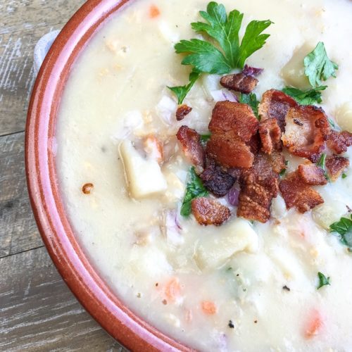 White creamy clam chowder topped with bacon and parsley in a soup bowl