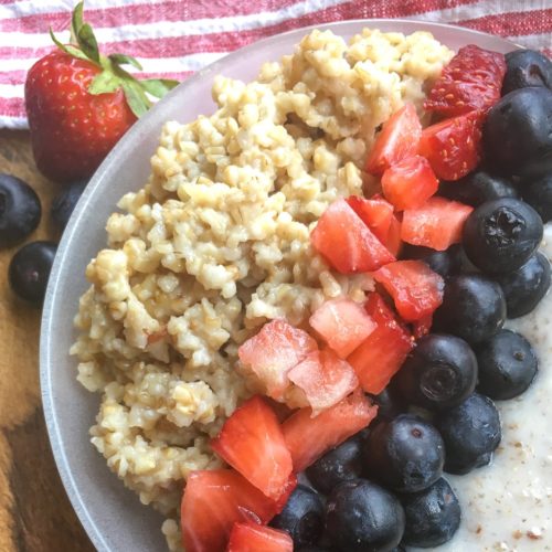 Cooked steel cut oats with yogurt, cut strawberries and blueberries