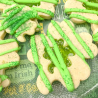 Close up of multiple Shamrock Sugar Cookies, with a green stained glass cut out, decorated with green icing and sprinkles
