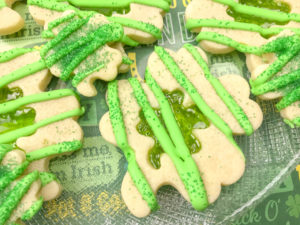 Close up of multiple Shamrock Sugar Cookies, with a green stained glass cut out, decorated with green icing and sprinkles