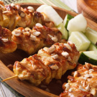 Chicken breasts on a skewer with peanut sauce and chopped peanuts on top on a wooden board