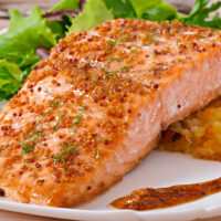 Salmon Fillet glazed with maple dijon sauce on a white plate with greens