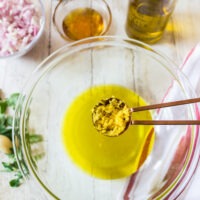 Adding lemon zest to olive oil and lemon juice in a glass mixing bowl