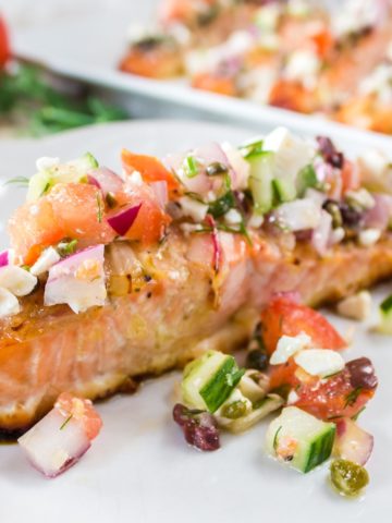 Baked Salmon with Greek Salsa on a white plate. Platter of salmon in the background