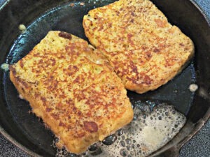 Two slices of bread soaked in egg cream mixture in a pan frying in butter until golden brown.