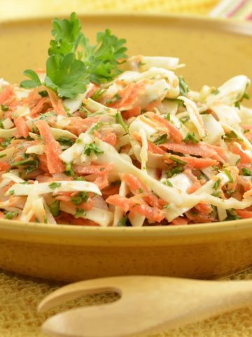 Shredded green and purple cabbage, carrots, with pineapple and cilantro in a large serving bowl with a wooden serving spoon.