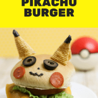 A Cheese burger on a bun decorated to look like Pikachu. 2 bugles are his ears, 2 slices of black olives are his eyes, two thin slices of pepperoni are his cheeks.
