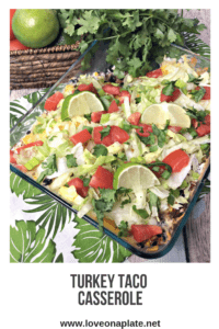 Glass Casserole dish topped with chopped lettuce, tomato, green onions and cilantro. Filling is ground turkey, black beans and corn.
