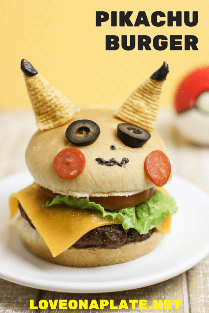 A Cheese burger on a bun decorated to look like Pikachu. 2 bugles are his ears, 2 slices of black olives are his eyes, two thin slices of pepperoni are his cheeks. 