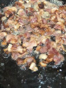 pieces of bacon being pan fried in a cast iron skillet