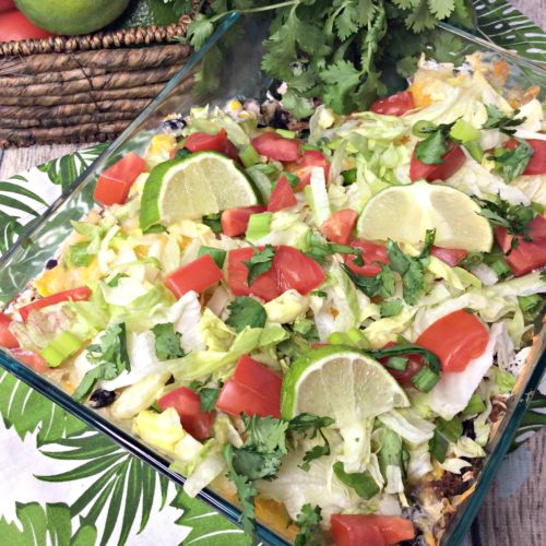 Glass Casserole dish topped with chopped lettuce, tomato, green onions and cilantro. Filling is ground turkey, black beans and corn.