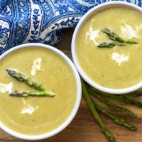 Two bowls of creamy Asparagus Soup, topped with asparagus tips and dollops of sour cream.