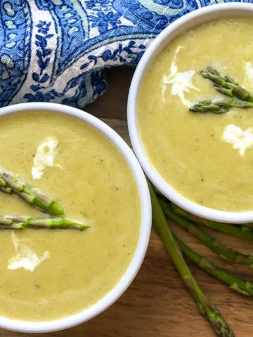 Two bowls of creamy Asparagus Soup, topped with asparagus tips and dollops of sour cream.
