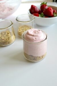 No bake strawberry cheesecake filling on top of graham cracker crumbs in a small serving size glass jar