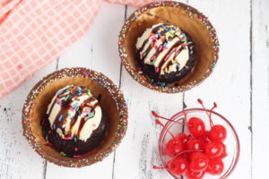Small waffle bowl, with freshly baked brownie, topped with ice cream, fudge syrup, whipped cream and a maraschino cherry