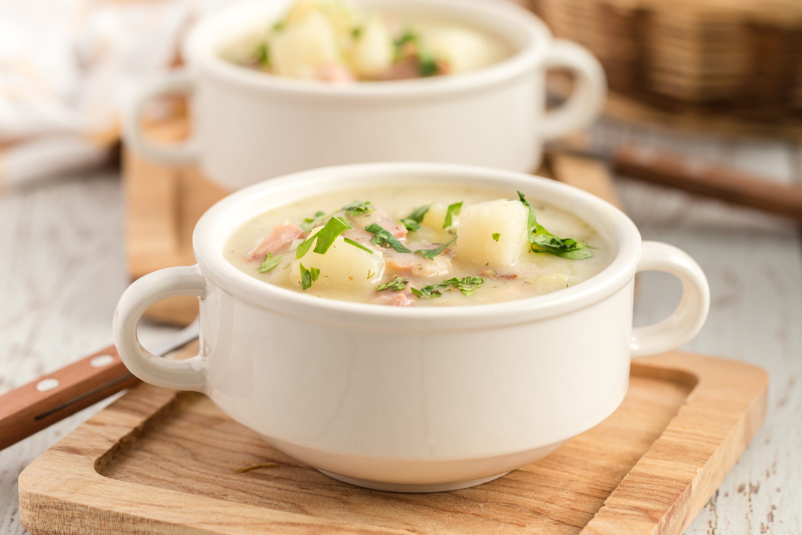 Cubes of potatoes and ham in a creamy white broth served in a white bowl topped with chopped  dill