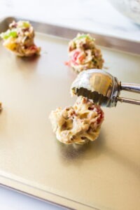 Dropping fruitcake cookie dough batter using a tablespoon onto a parchment lined cookie sheet
