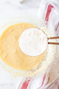Adding flour to a glass bowl of Fruitcake cookie dough