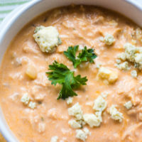 Close up of Buffalo Chicken Soup in a white bowl with crumbled blue cheese and a sprig of parsley