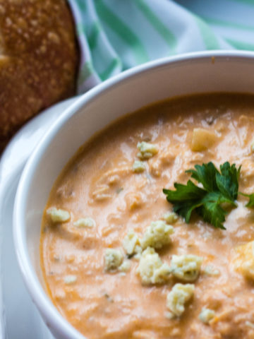Creamy Buffalo Chicken Soup is a large white bowl with sourdough bread and celery sticks