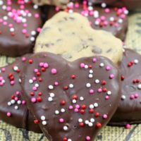 A styled pile of chocolate covers heart shaped cookie dough truffles.