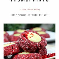 Red Velvet Thumbprint cookies rolled in sanding sugar and filled with cheesecake on a white cookie platter.