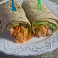 Buffalo Chicken filling in a wrap with lettuce, tomatoes, red onions. Wrap is cut in half and filling is showing.
