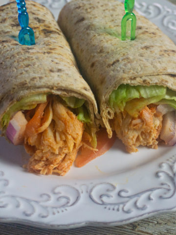 Buffalo Chicken filling in a wrap with lettuce, tomatoes, red onions. Wrap is cut in half and filling is showing.
