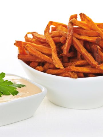 A bowl of crisp sweet potato fries and a small white bowl of fry sauce with parley on top