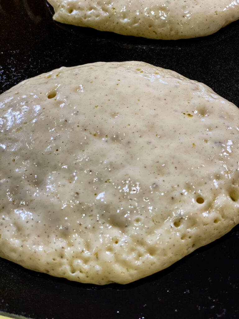 Sourdough pancake batter with bubbles cooking on a griddle