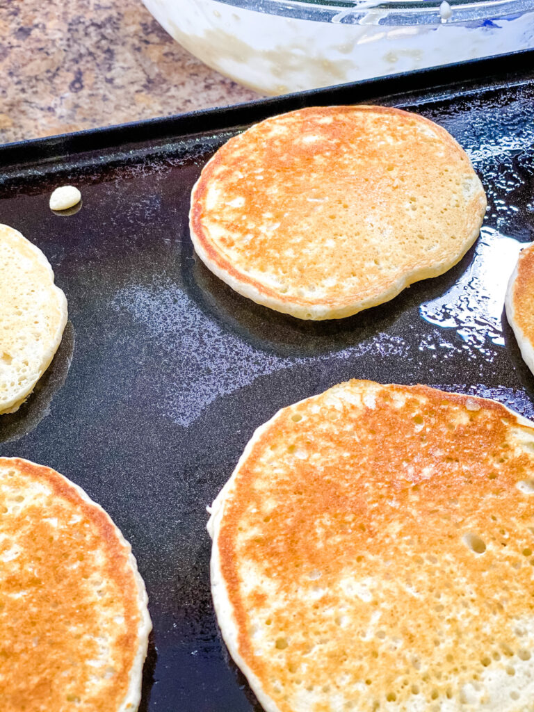 Golden brown sourdough pancakes cooking on a griddle