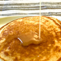 Closeup of 2 sourdough pancakes with syrup being drizzled on to them