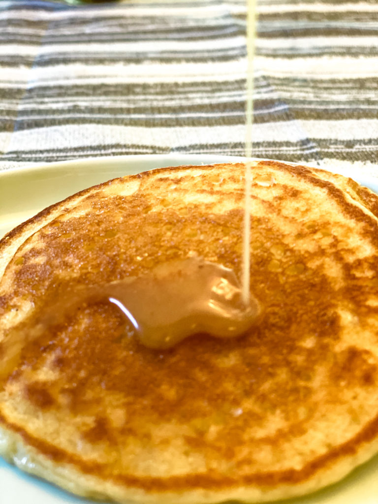 Closeup of 2 sourdough pancakes with syrup being drizzled on to them