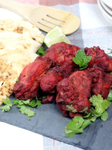 pieces of Tandoori chicken on a slate platter with pieces of naan cut into quarter
