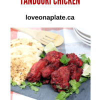 pieces of Tandoori chicken on a slate platter with pieces of naan cut into quarter