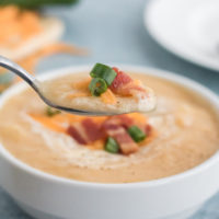 Instant Pot Potato Soup recipe, chicken broth, potatoes, onions, thyme and cream cooked in the Instant Pot and loaded with cooked bacon, spring onions, and cheese. Served in a ceramic white bowl